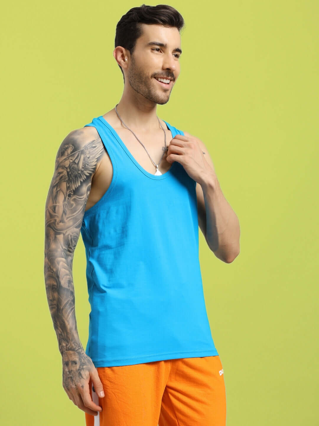 Alt Tag: Man wearing bright blue Bonny Gym T-shirt, displaying tattooed arm, styled with orange shorts against green background.