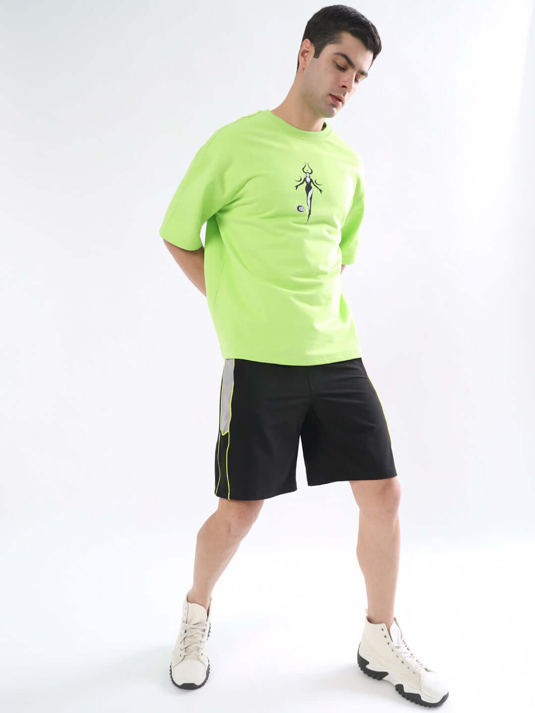 Man wearing Boomer Shorts in black with neon green piping, paired with neon green t-shirt and white sneakers, showcasing casual style.