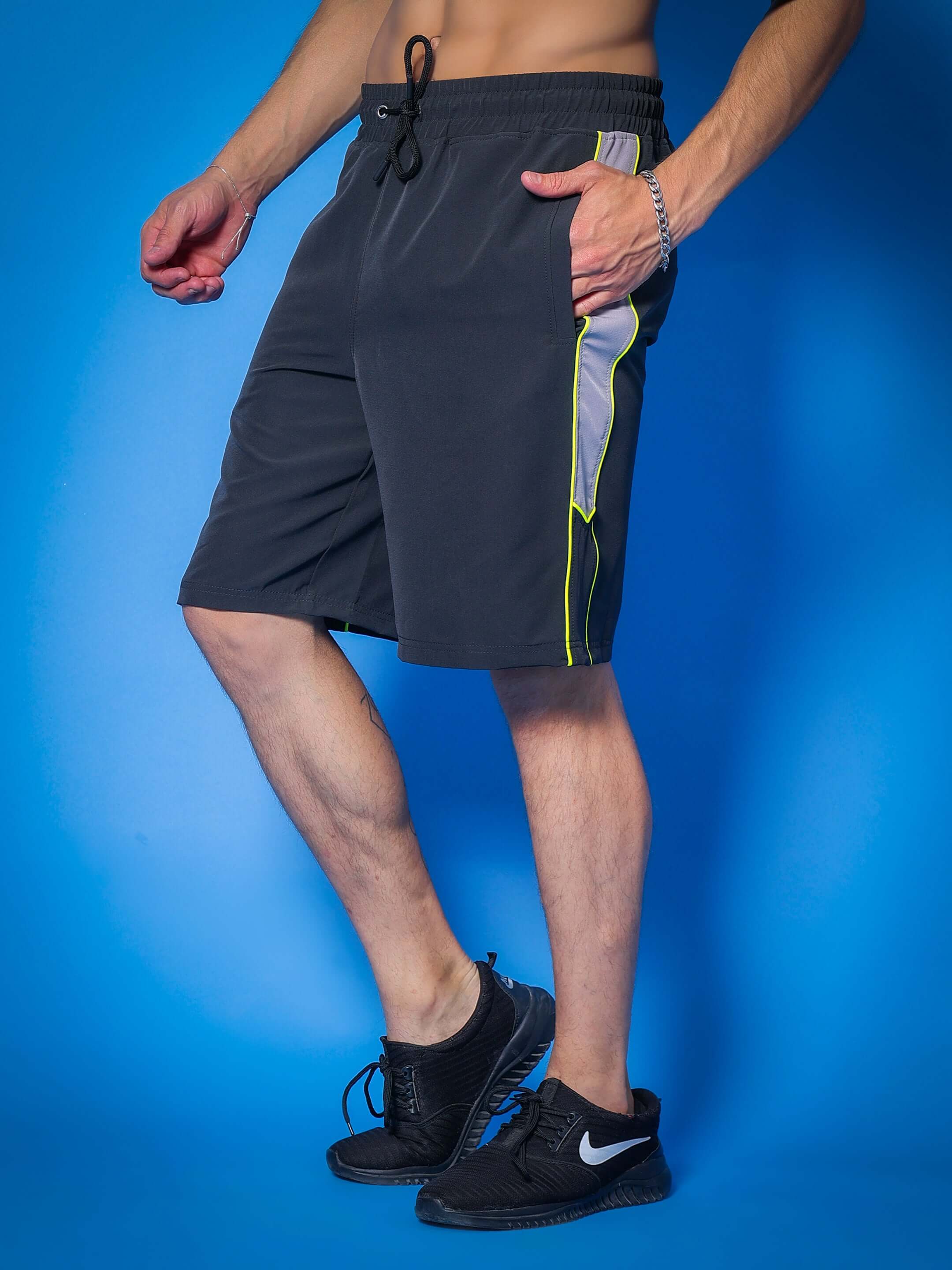 Dark grey Boomer shorts with neon green piping, customizable fit option available for prepaid orders, modeled on a blue background.