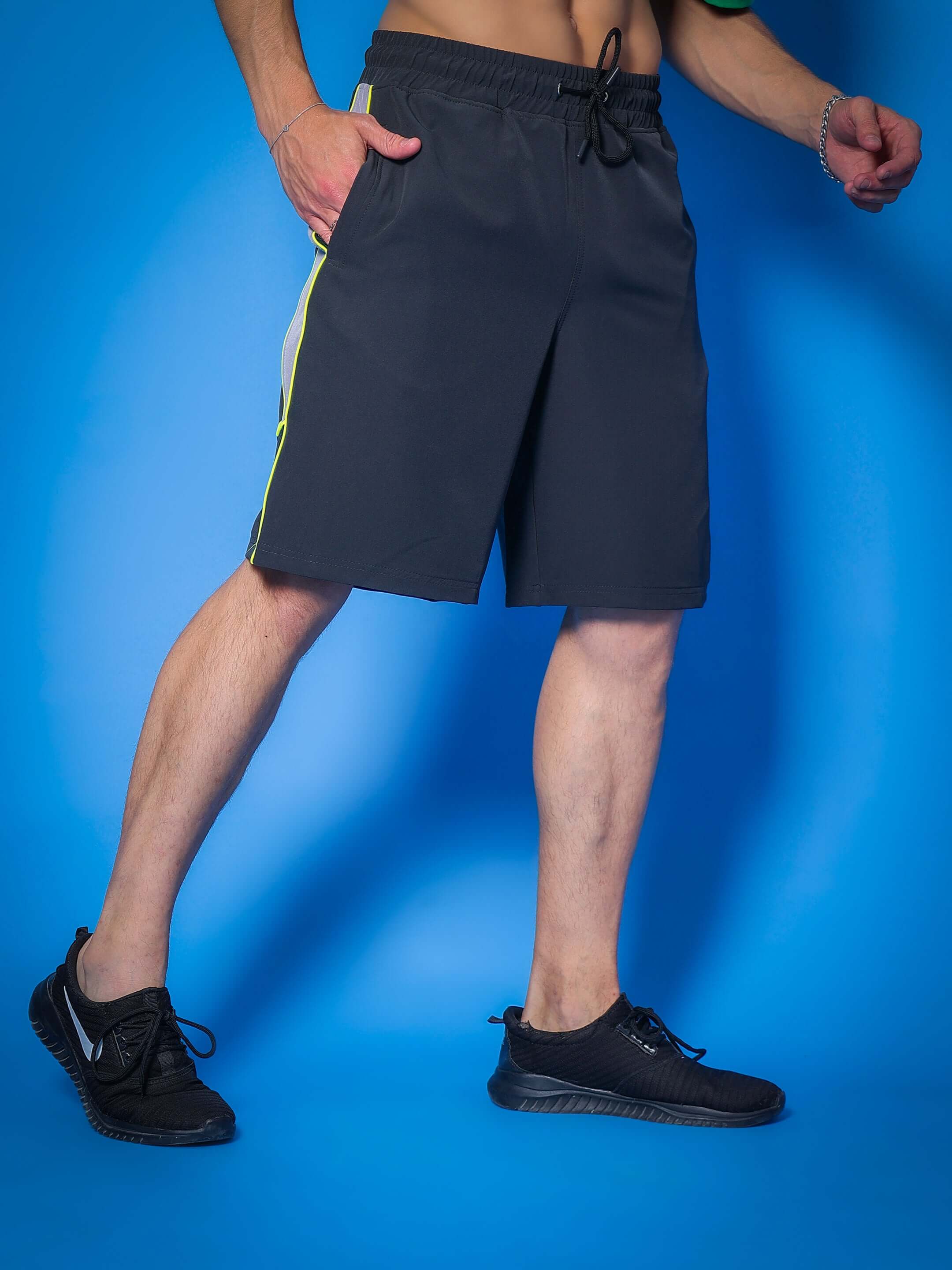 Model wearing Boomer Shorts in dark grey with neon green piping, showcasing sporty style and customizable fit options.