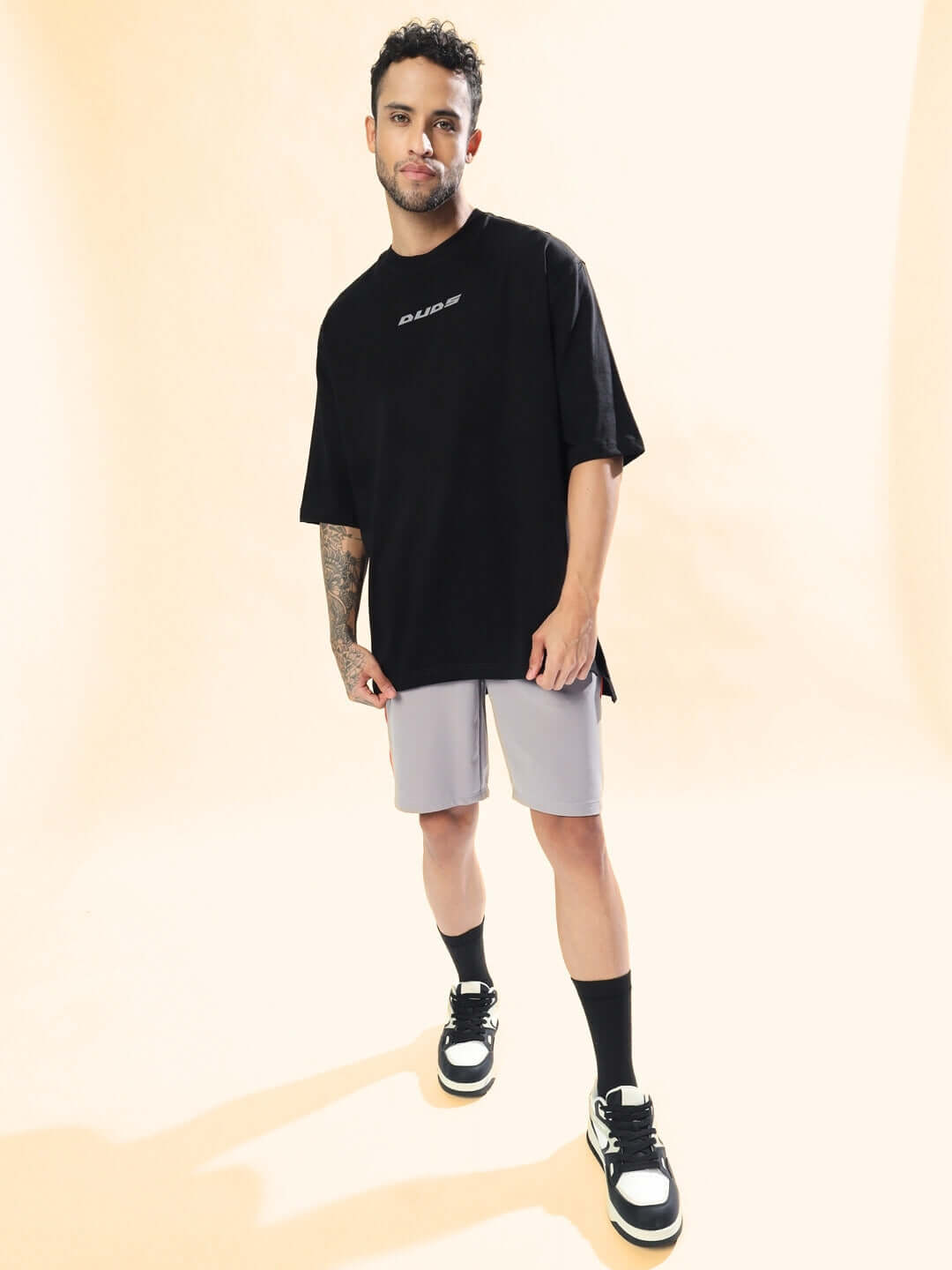 Man wearing BOOMER SHORTS GREY WITH ORANGE PIPING, paired with a black t-shirt and sneakers, showcasing sporty and casual style.