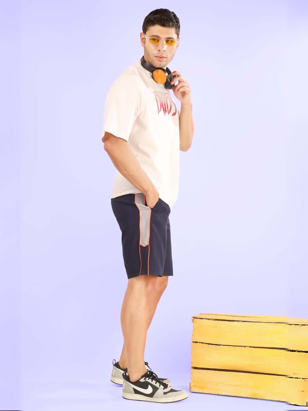 Model wearing BOOMER SHORTS NAVY WITH ORANGE PIPING paired with streetwear on a pastel background, showcasing vibrant orange piping.