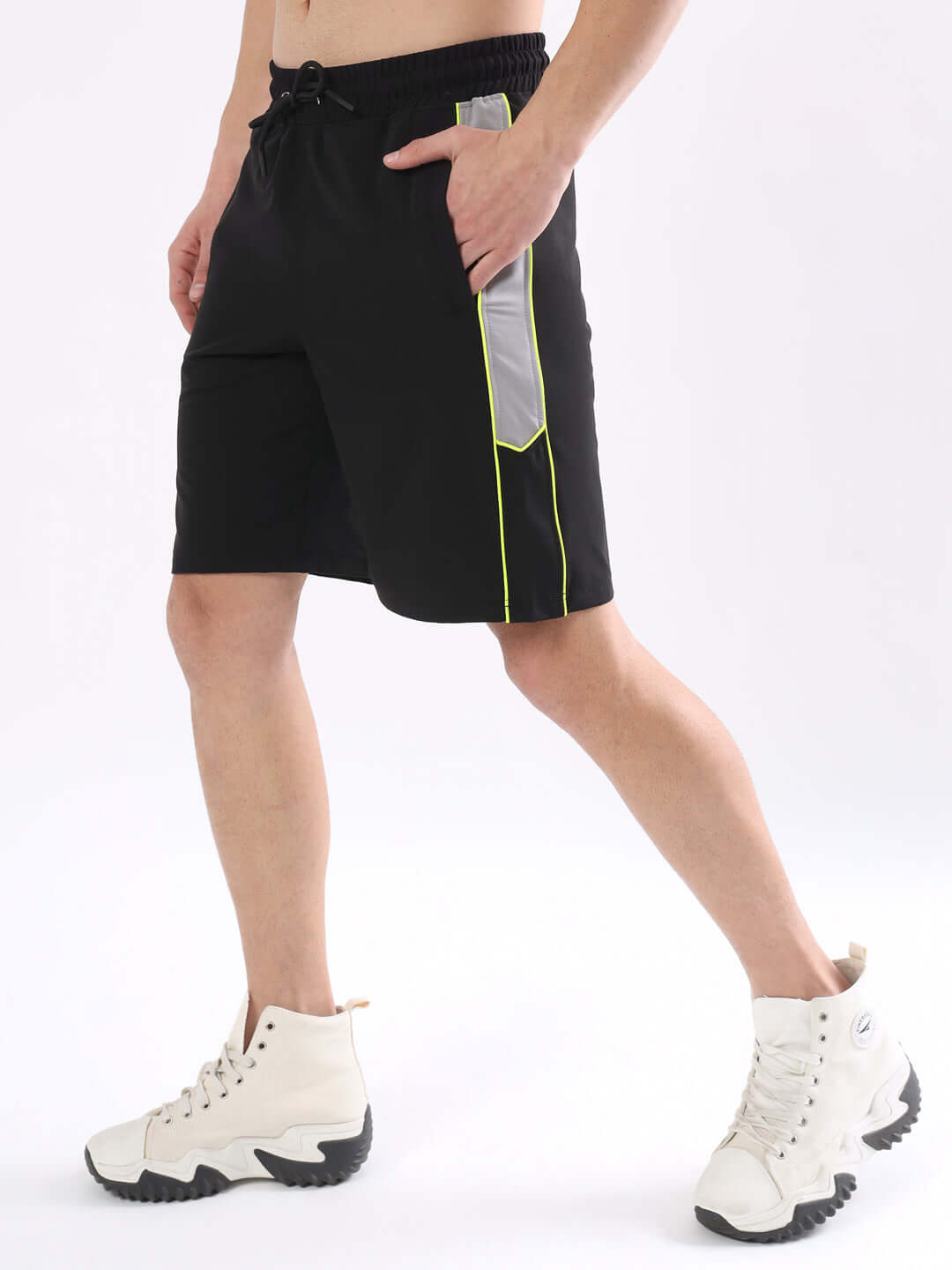 Model wearing Boomer black shorts with neon green piping, paired with white high-top sneakers, highlighting side detail and style.