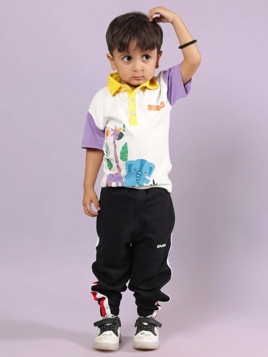 Young child wearing BORNEO CO-ORD FOR BOYS & GIRLS OFF WHITE-BLACK outfit, featuring a colorful top and black pants, posing against a light purple background.