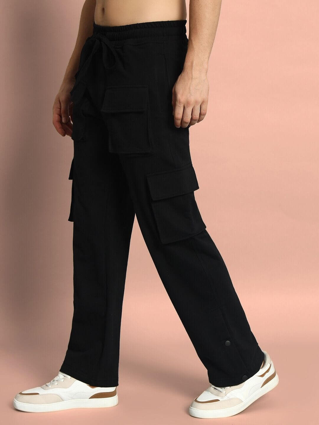 Person wearing black cargo pants with multiple pockets paired with white sneakers against a neutral backdrop.