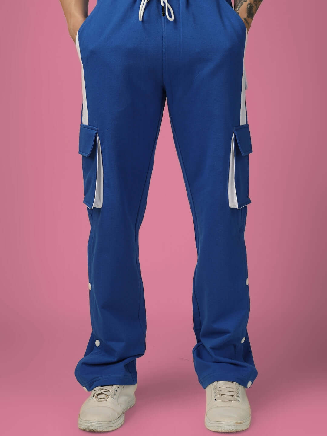 Front view of blue cargo pants with white highlights, featuring multiple pockets and adjustable fit on a pink background.
