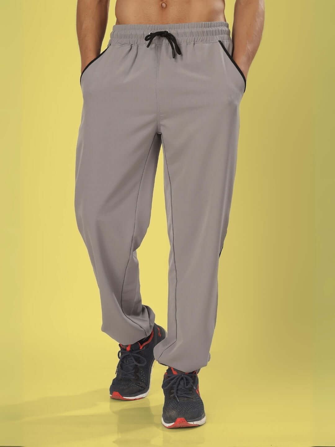 Model wearing BRAVO relaxed fit grey cargo pants with drawstring waist, shown on a yellow background, emphasizing comfort and style.