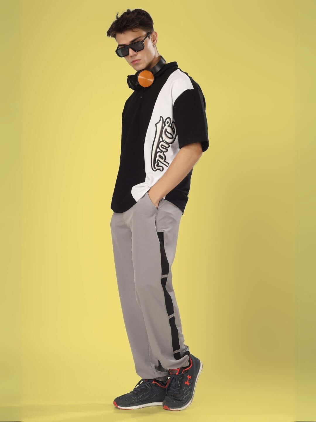 Man wearing Bravo Relaxed Fit Grey Cargo Pants with black and white shirt, standing stylishly against yellow background.