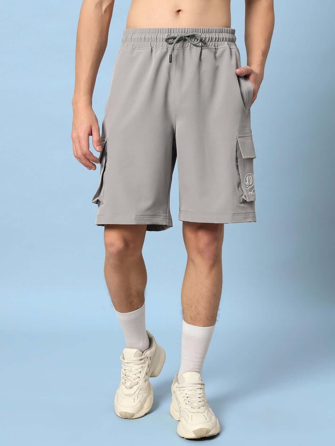 Brawny grey cargo shorts with pockets, ideal for custom fit options, worn by a model with white sneakers on a light blue background.