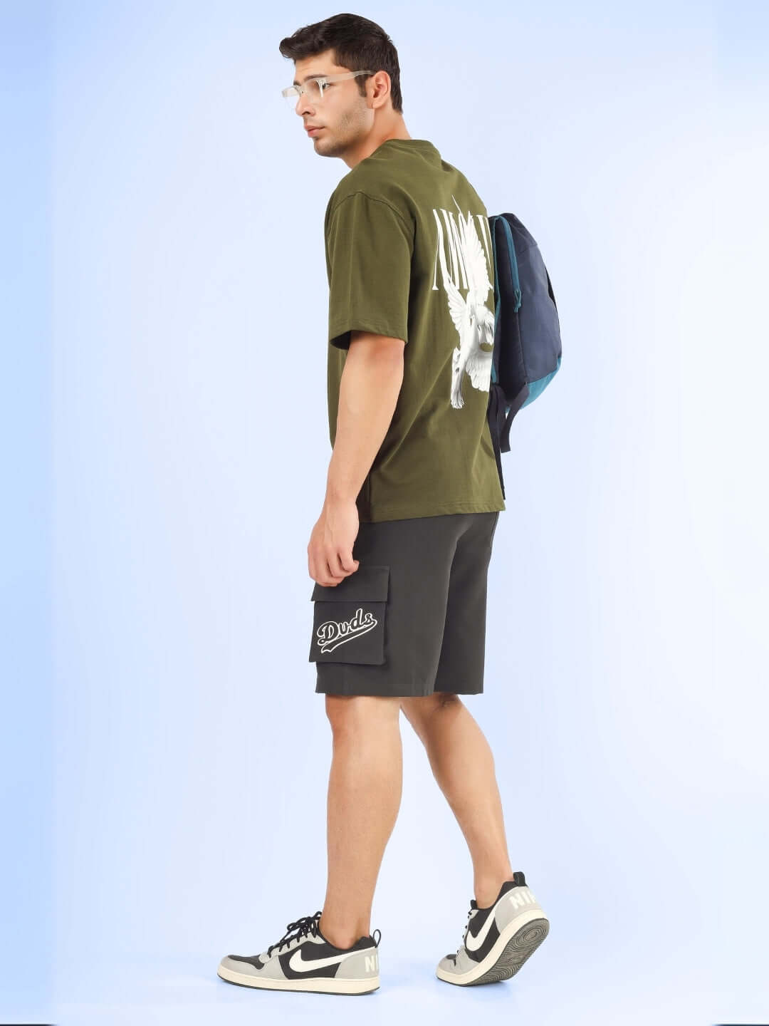 Man wearing Brawny Cargo Shorts in dark grey with a green shirt and backpack, showcasing style and comfort.