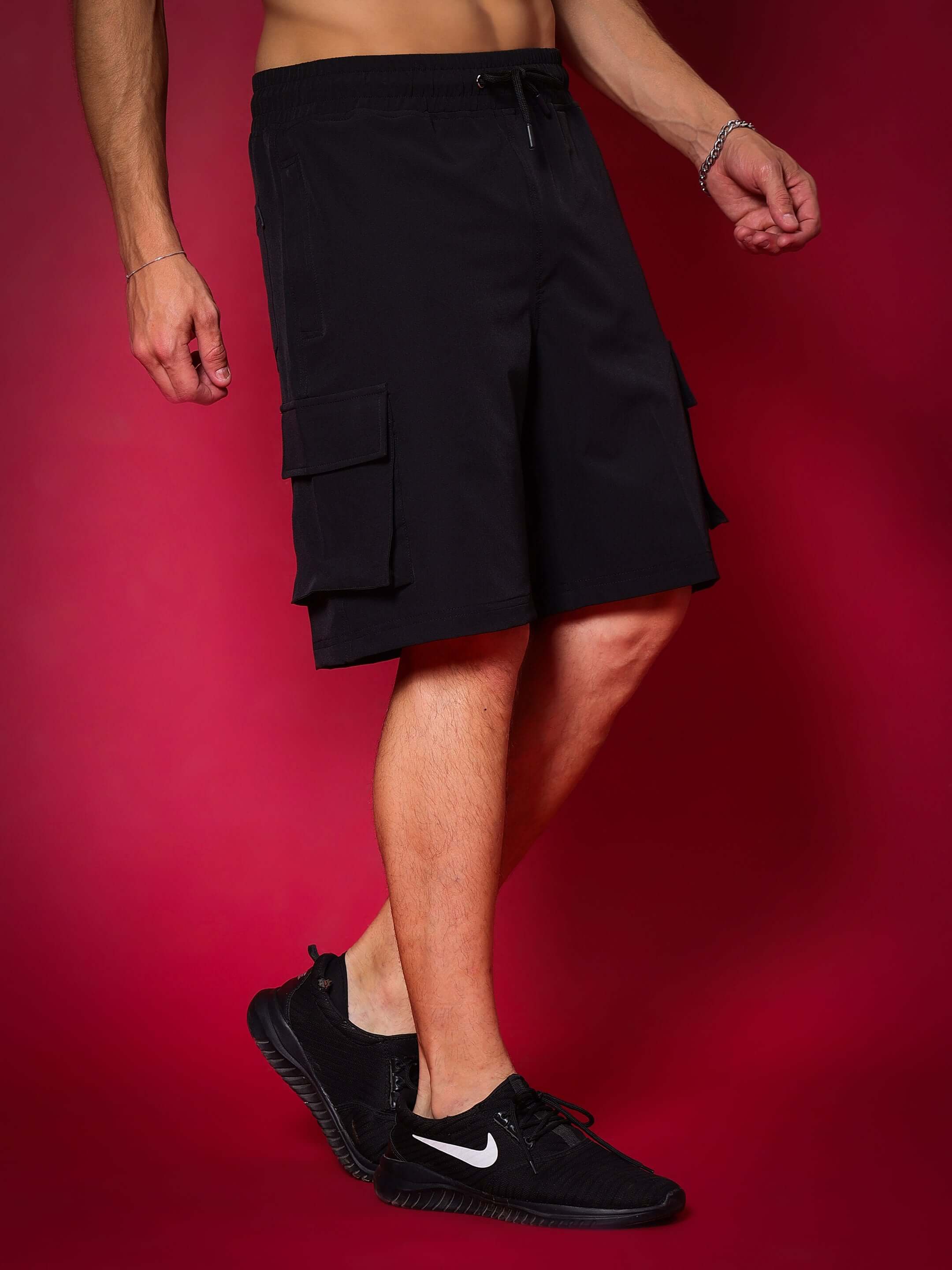 Man wearing black Brawny cargo shorts with pockets against a red background, showcasing casual fashion and sporty design.
