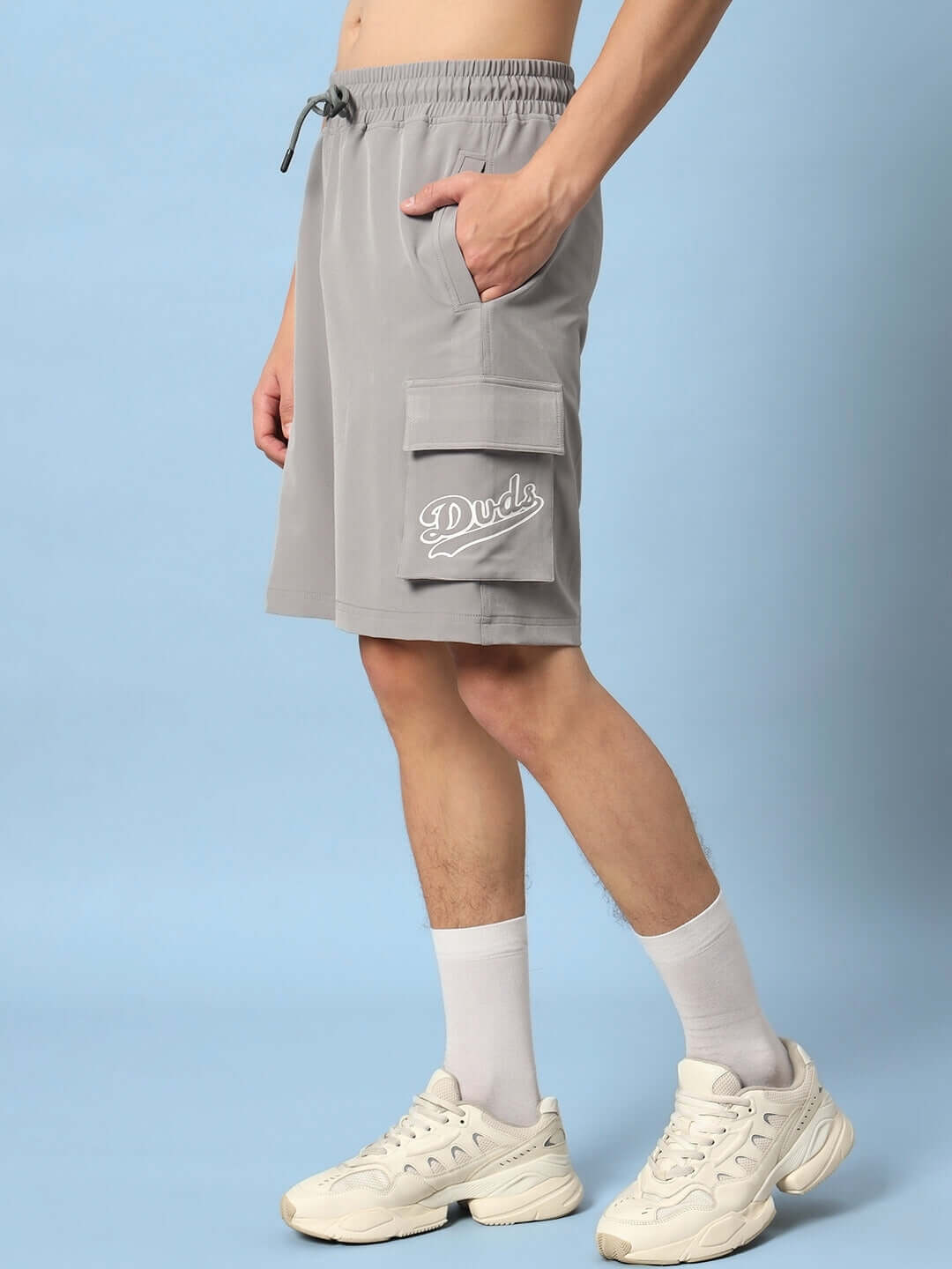 Person wearing grey Brawny cargo shorts with pockets, showcasing casual style, customizable fit option available, DUDS branding visible.