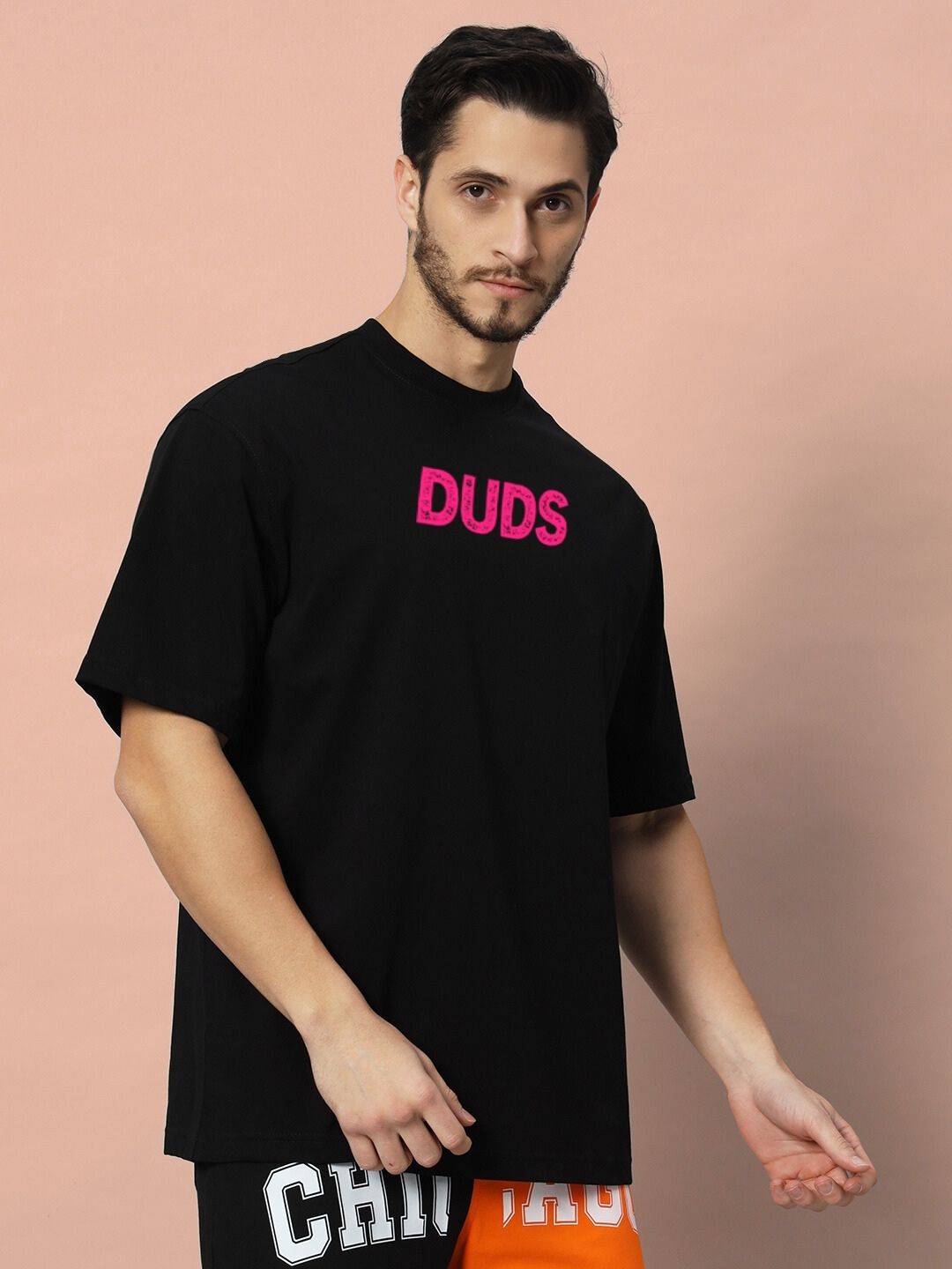 Man wearing BREAKING OVER-SIZED T-SHIRT BLACK with pink 'Duds' text