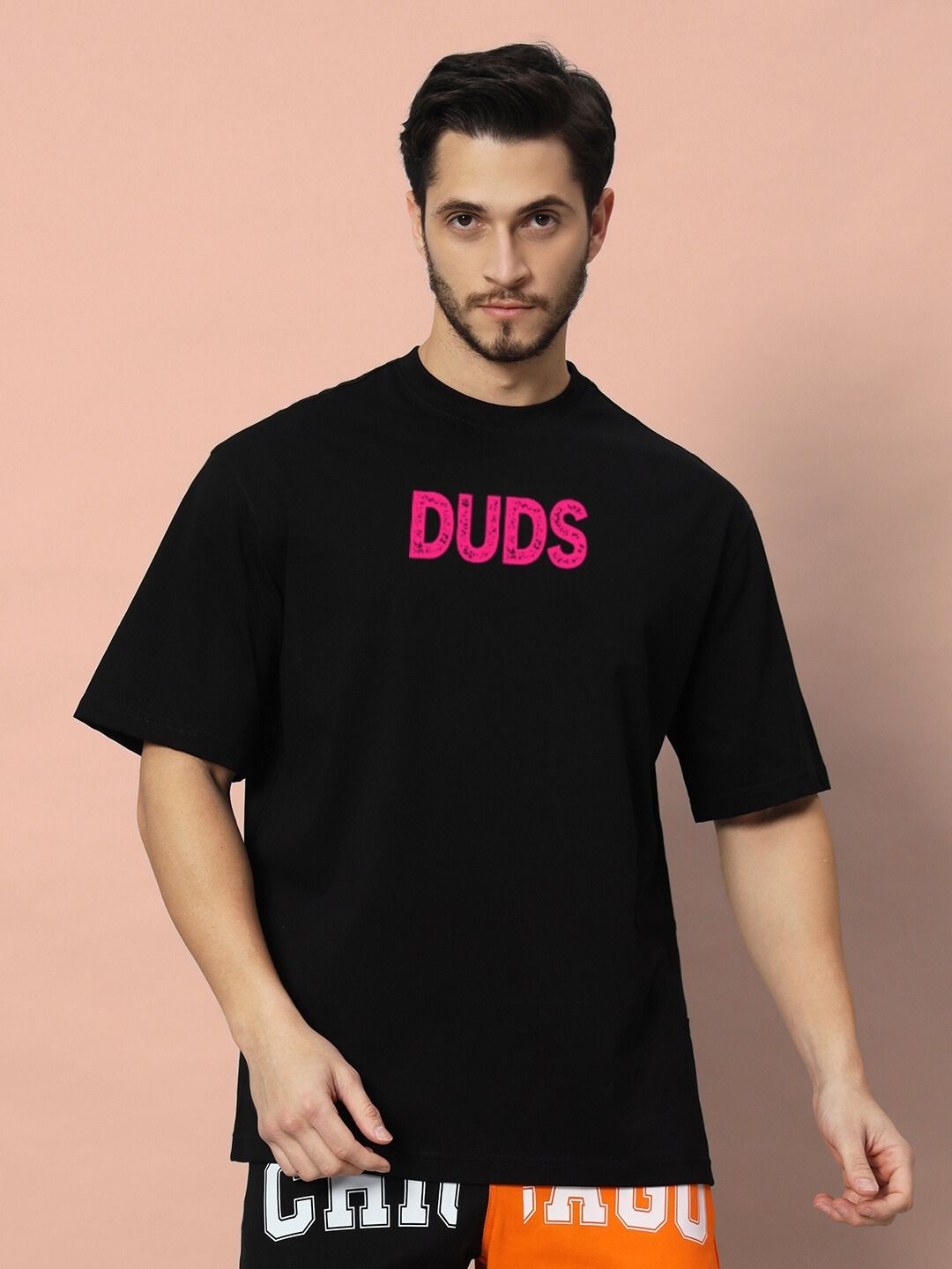 Model wearing BREAKING OVER-SIZED T-SHIRT BLACK with bold pink 'DUDS' print, showcasing comfortable and stylish casual wear.