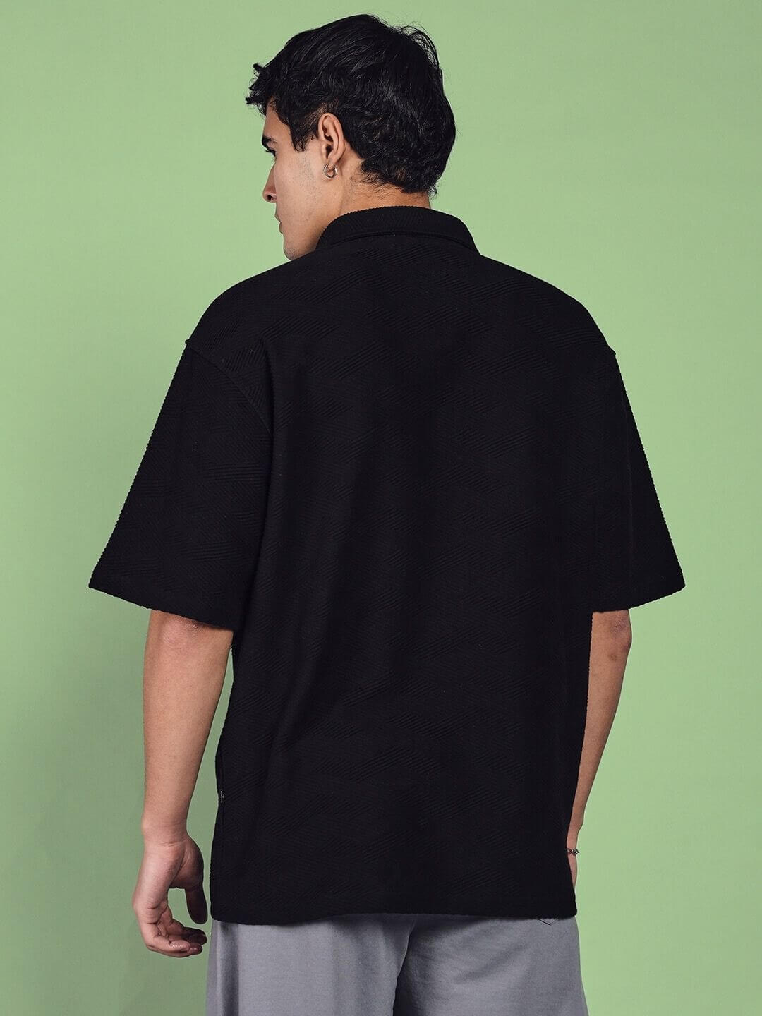Man wearing BROCADE POLO COTTON T-SHIRT BLACK, showcasing the back design against a green background.