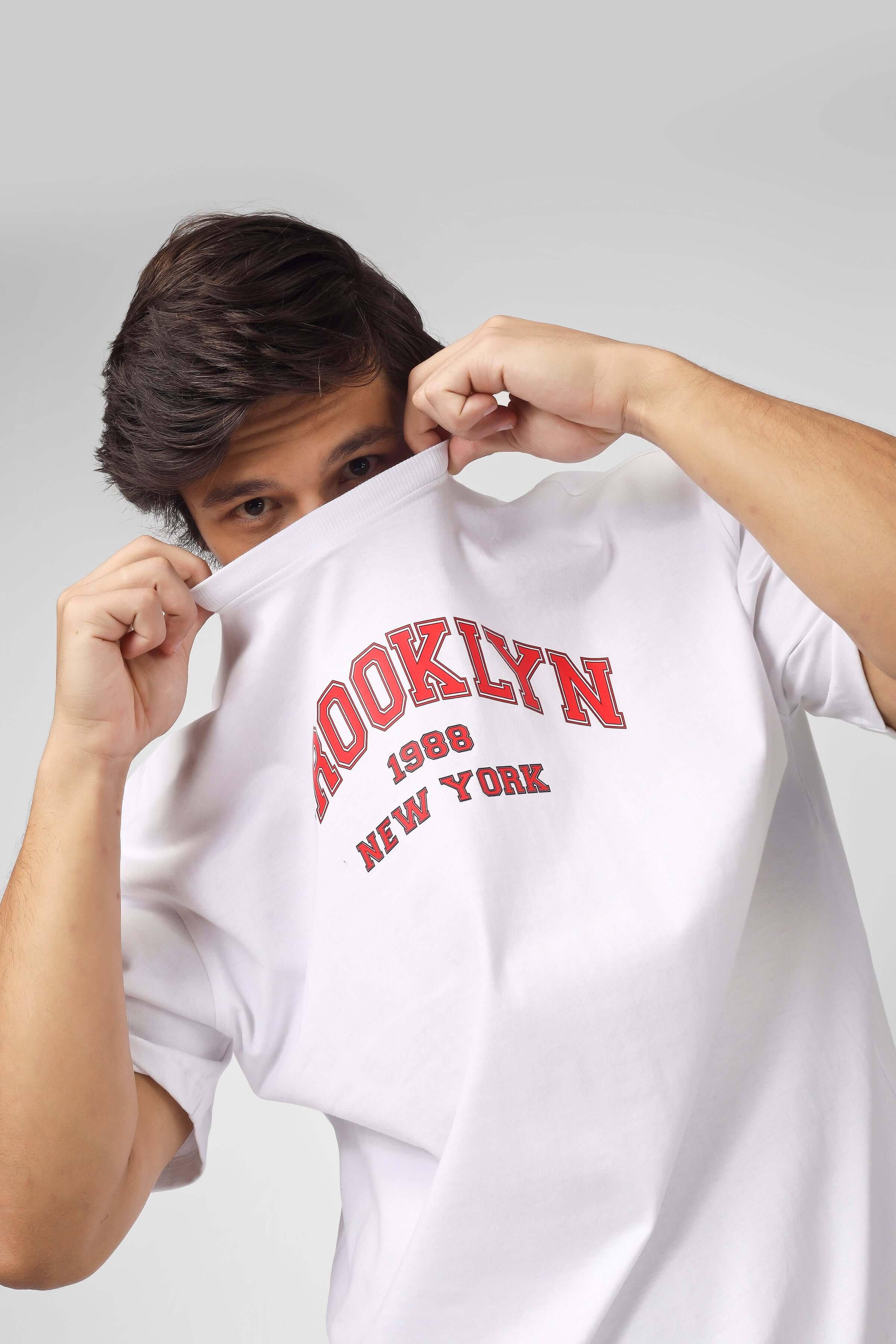 Person wearing Brooklyn Co-Ord Set white and red shirt, lifting collar over face, showcasing 1998 New York text design