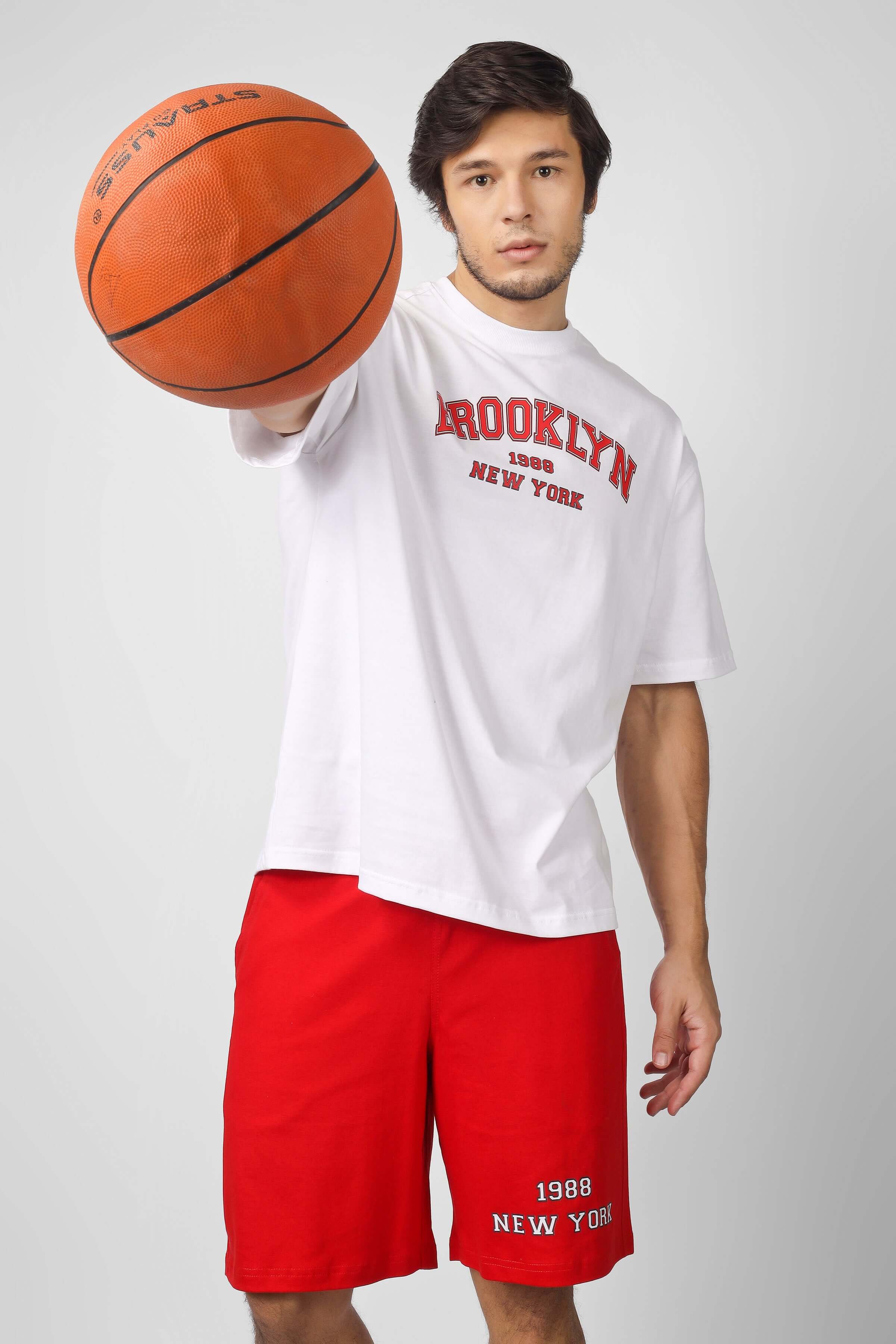 Model wearing Brooklyn Co-Ord Set in white and red, holding basketball, showcasing casual sportswear style.