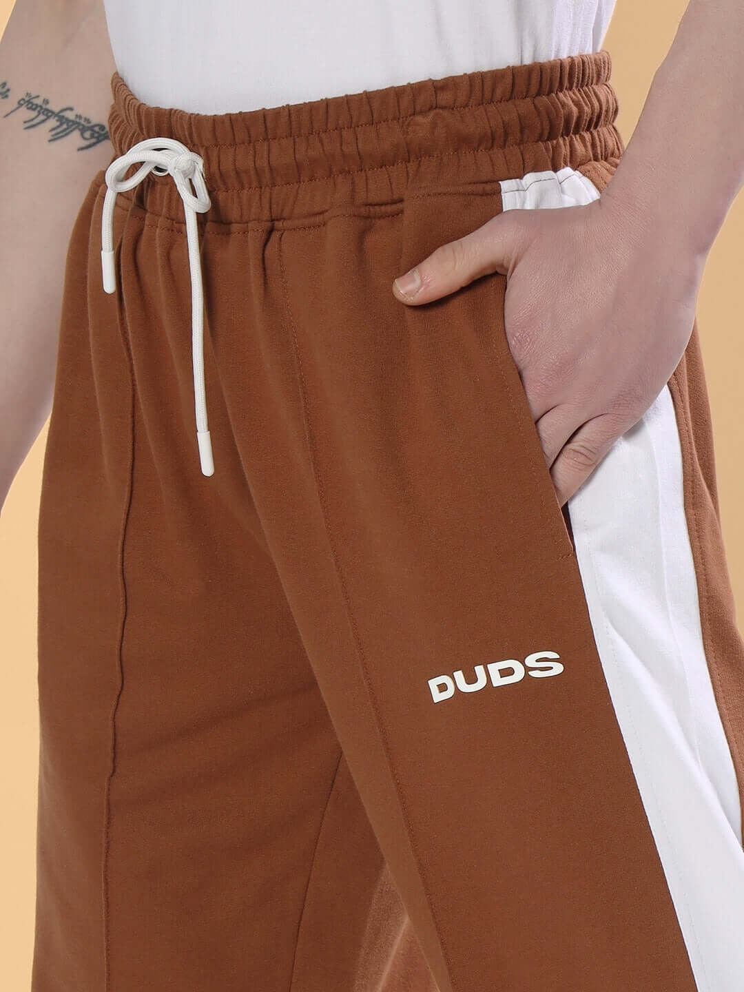Close-up of a person wearing brown side seam plated joggers with a drawstring waist and branding, custom fit options available at DUDS.