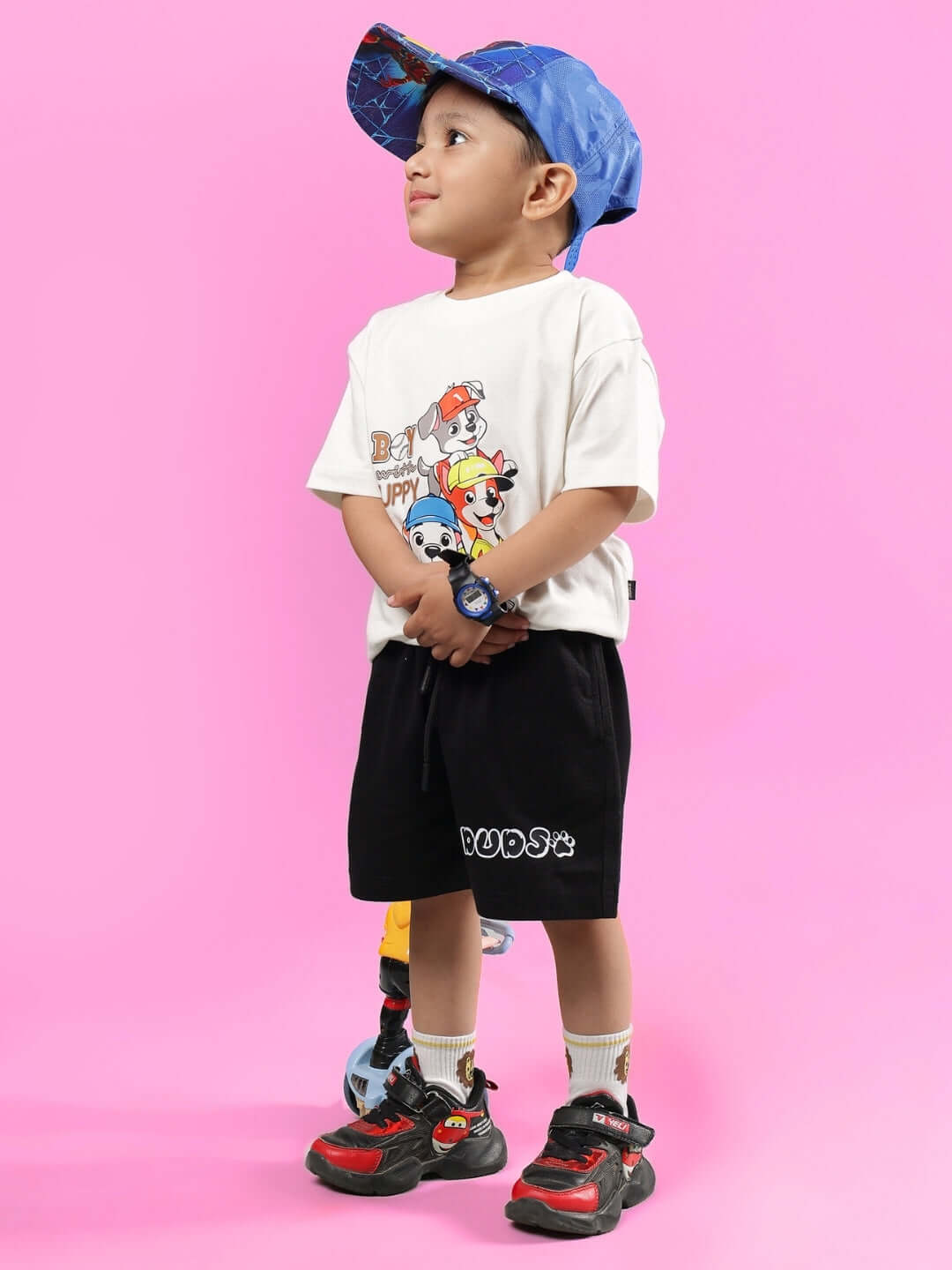 Young child wearing BRUNO CO-ORD FOR BOYS & GIRLS OFF WHITE-BLACK outfit with blue cap on pink background