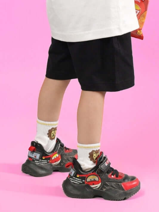 Child wearing BRUNO SHORTS FOR BOYS & GIRLS BLACK, standing on a pink background, displaying the comfortable fit and vibrant style.