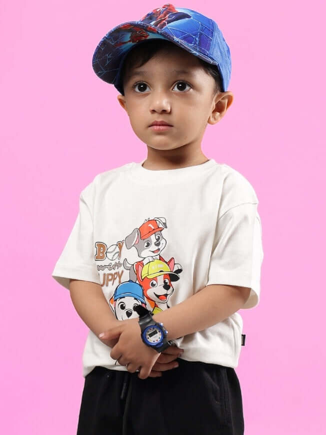 Young child wearing a blue cap and an off-white BRUNO oversized T-shirt with cartoon design, against a pink background.