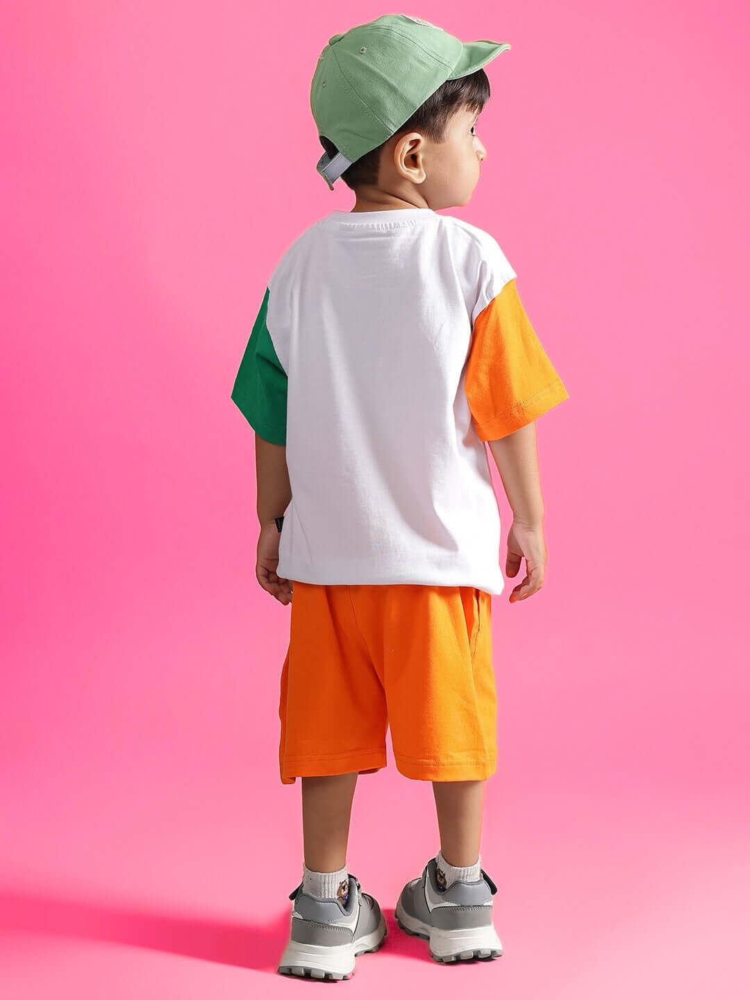 Young child wearing BUDDY CO-ORD FOR BOYS & GIRLS WHITE-ORANGE outfit, standing against a pink background.