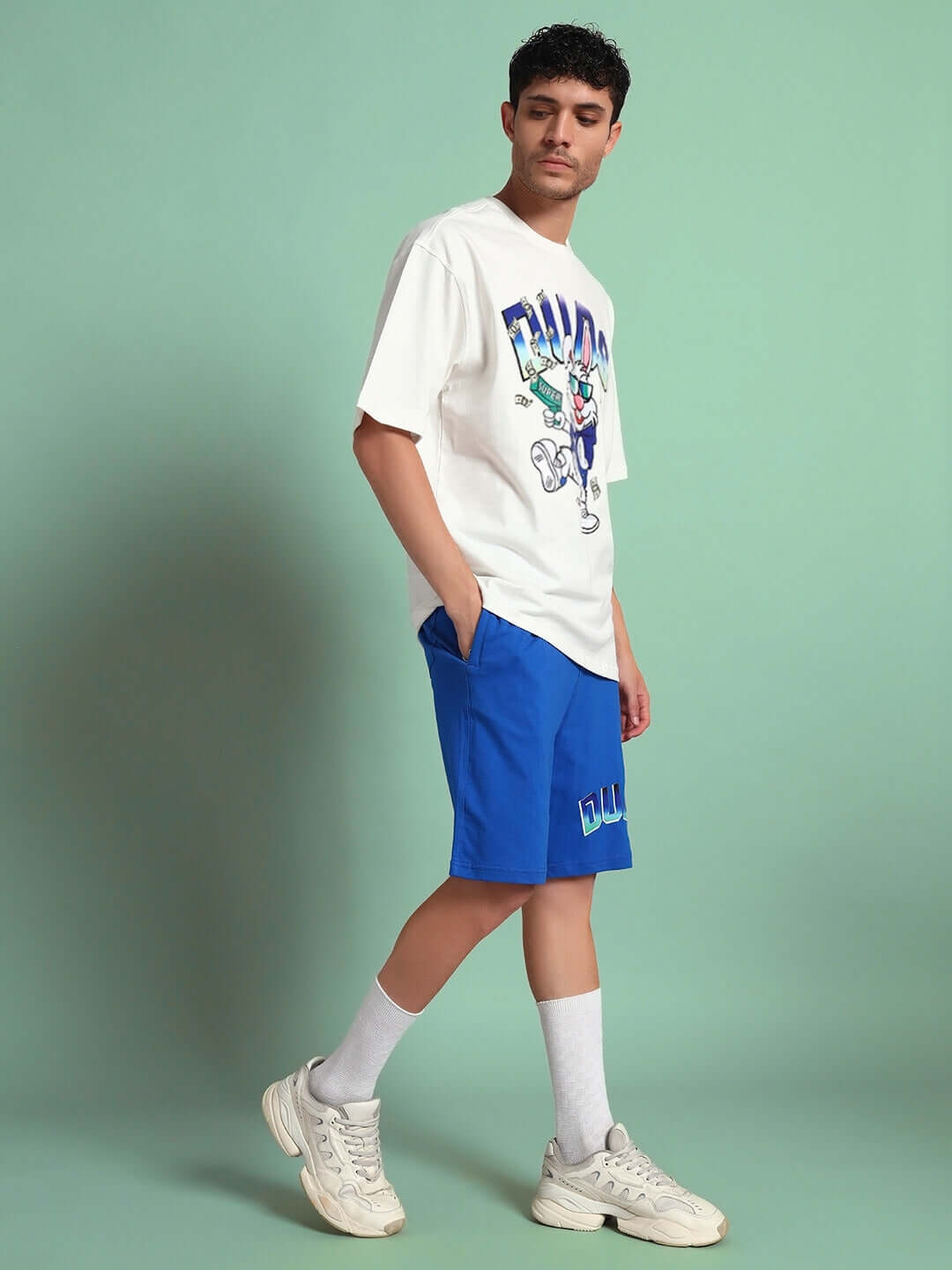 Man wearing Bunny Bugs Co-Ord Set in off-white and blue, featuring a premium cotton and elastane blend, standing against a green background.