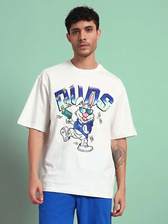 Man wearing an off-white oversized T-shirt with a cartoon bunny graphic, styled with blue shorts, standing against a green background.