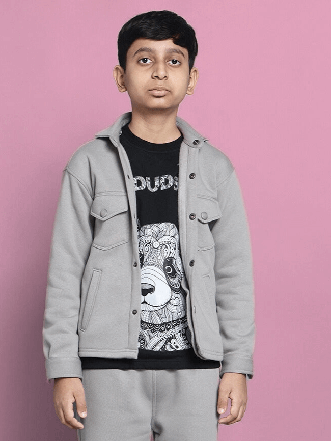 Young boy wearing a grey fleece sweatshirt with a graphic t-shirt, standing against a pink background.
