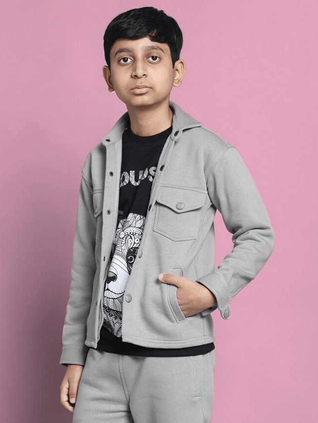 Boy wearing grey fleece sweatshirt standing against a pink background