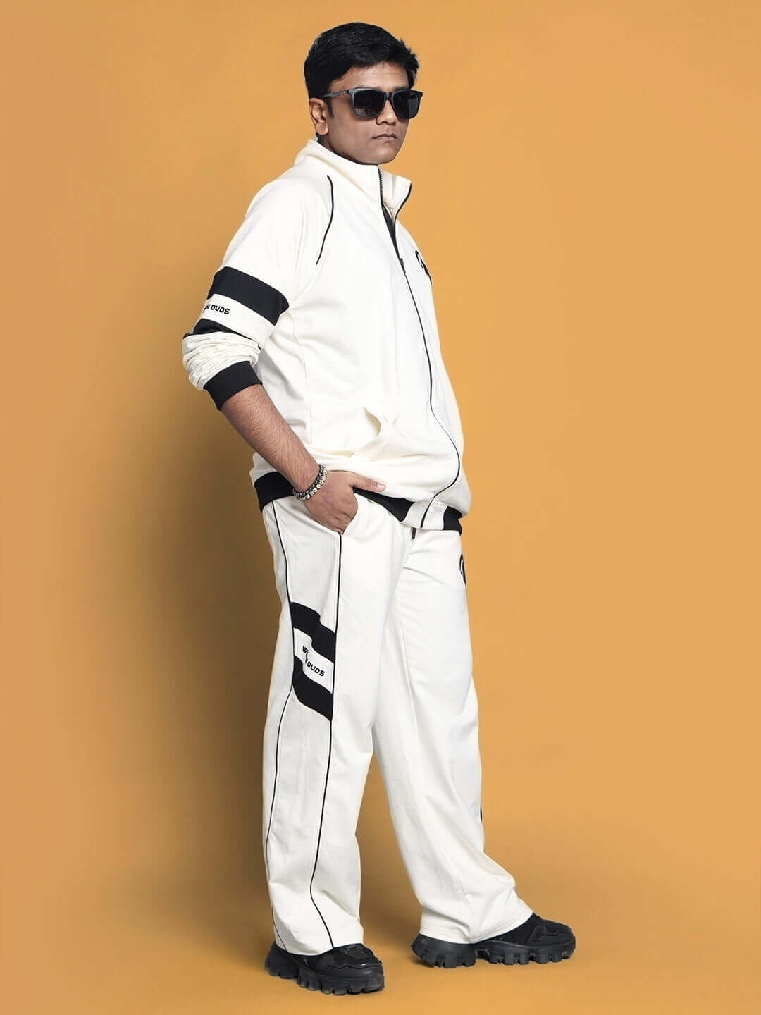 Model wearing CALEDONIA CO-ORD SET in off white, premium cotton material with sporty black accents, standing against a mustard background.