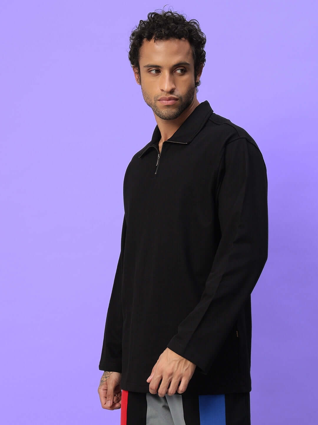Man wearing a black oversized sweatshirt with a collar, posing against a purple background, showcasing casual streetwear style.
