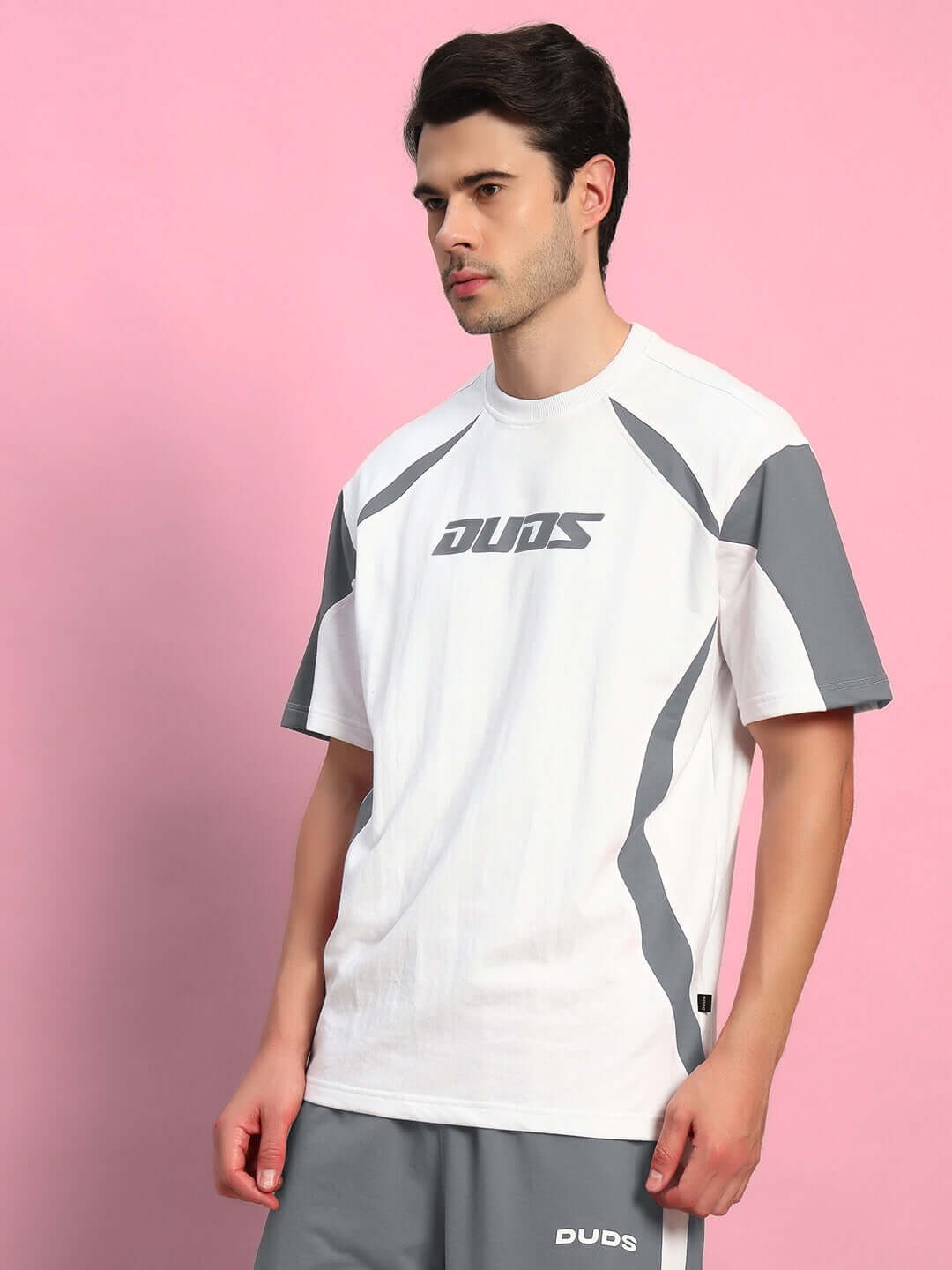 Model wearing Candor oversized T-shirt in white grey, made from premium cotton French terry with elastane, standing against pink background.