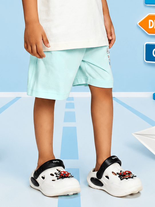CARTOON BEAR SHORTS FOR BOYS GIRLS MINT GREEN worn with cute clogs against a colorful background.