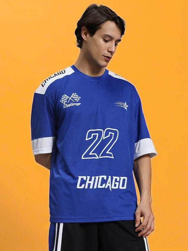 Man wearing CHALLENGE OVER-SIZED T-SHIRT ROYAL BLUE with Chicago print, posing against an orange background.