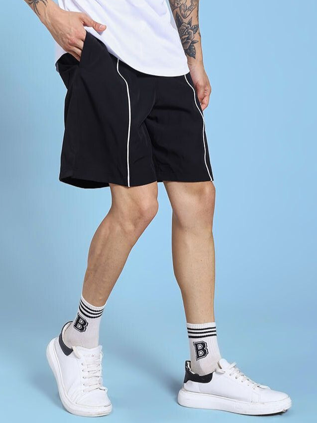 Man wearing CHAMPION ZONE FRONT PLATED SHORTS BLACK with white sneakers on blue background, showcasing sporty style and functionality.
