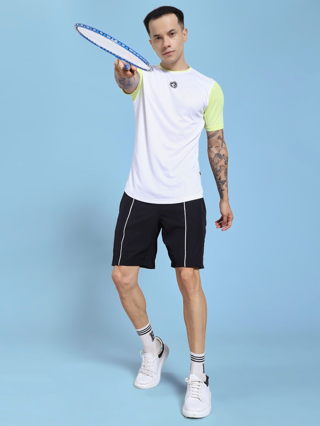 Man playing with tennis racket wearing CHAMPION ZONE REGULAR FIT CO-ORD SET WHITE NEON BLACK with sporty design in a blue background.