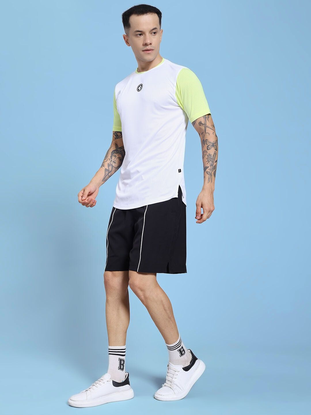 Man wearing CHAMPION ZONE REGULAR FIT CO-ORD SET WHITE NEON BLACK showcasing sporty streetwear fashion against a blue background.