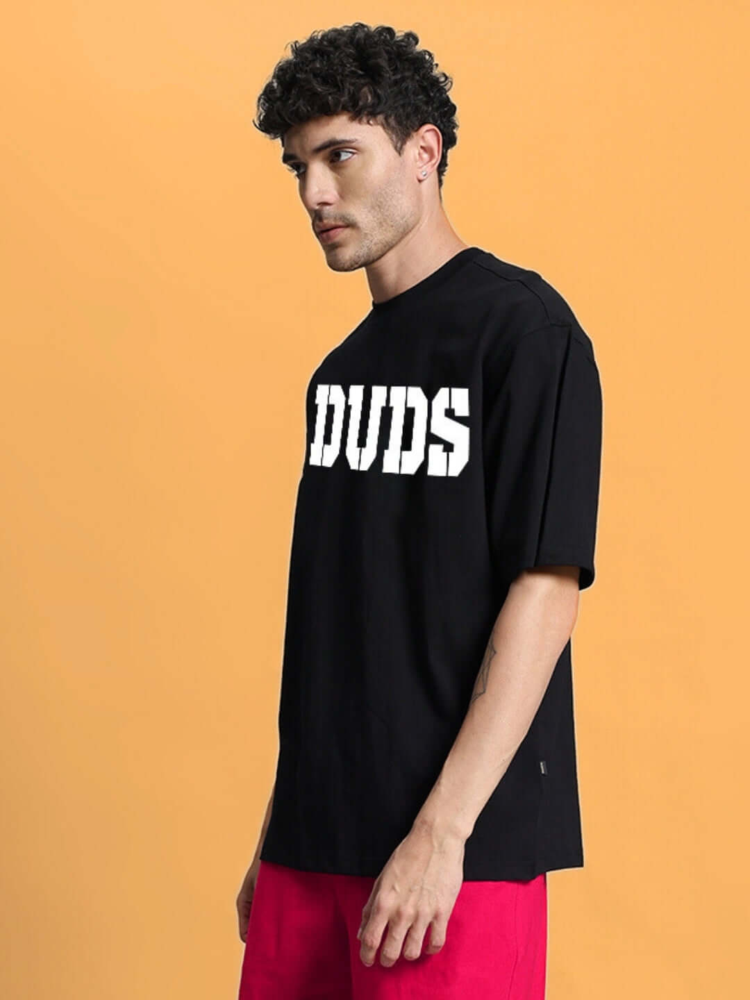 Model wearing CHERRY BLOSSOM OVER-SIZED T-SHIRT BLACK with bold white text design on the front, paired with red pants.