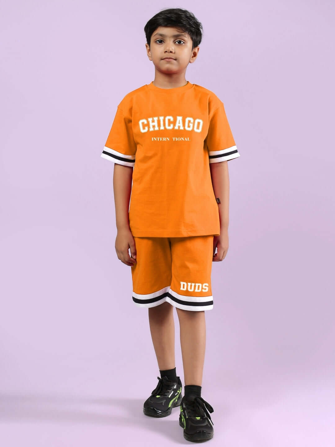 Child wearing orange Chicago printed co-ord set from DUDS, featuring a T-shirt and shorts with black sneakers.