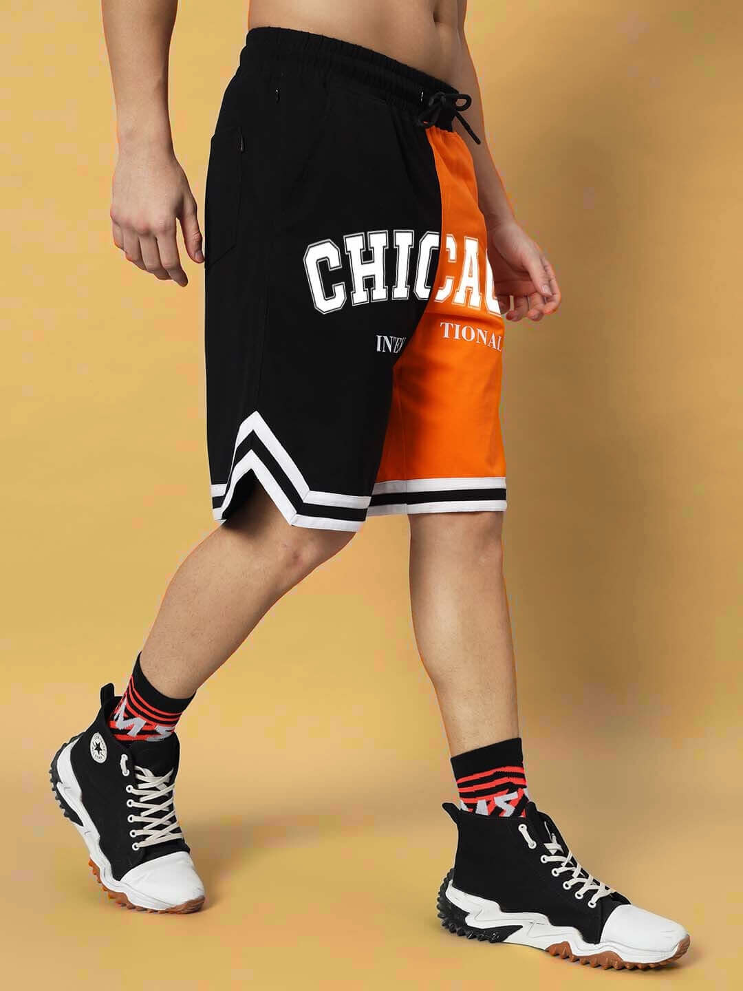 Person wearing Chicago regular fit shorts, orange-black with custom fit option, styled with black sneakers.