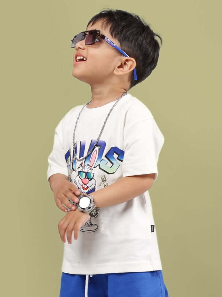 Child wearing off-white Bumble T-shirt for kids with a playful design, sunglasses, and blue shorts, showcasing trendy apparel by DUDS.