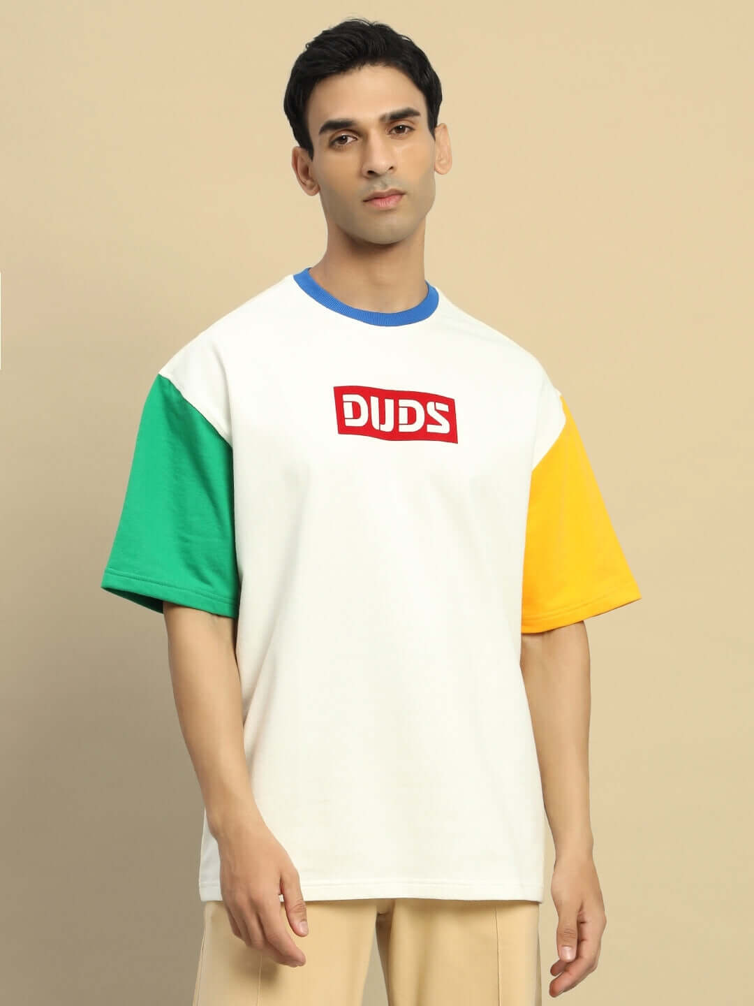 Model wearing Chroma Color Blocked Oversized T-Shirt in off white with green and yellow sleeves, DUDS logo on chest, beige background.