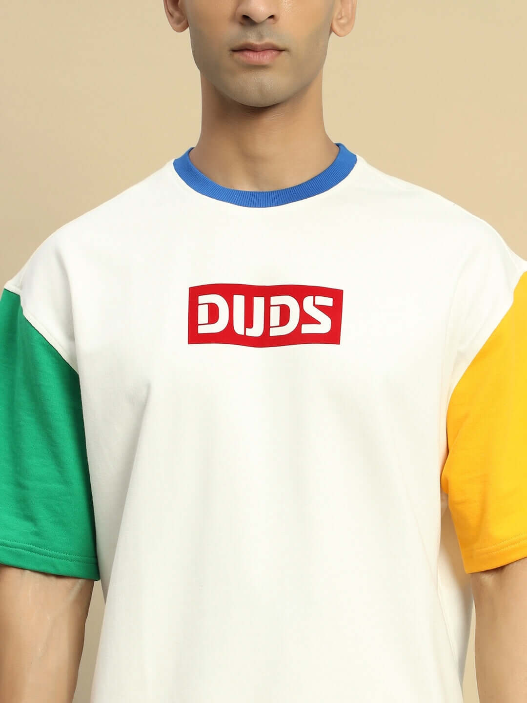 Unisex off-white oversized t-shirt with green and yellow color blocking, blue neckline, and red logo on chest.