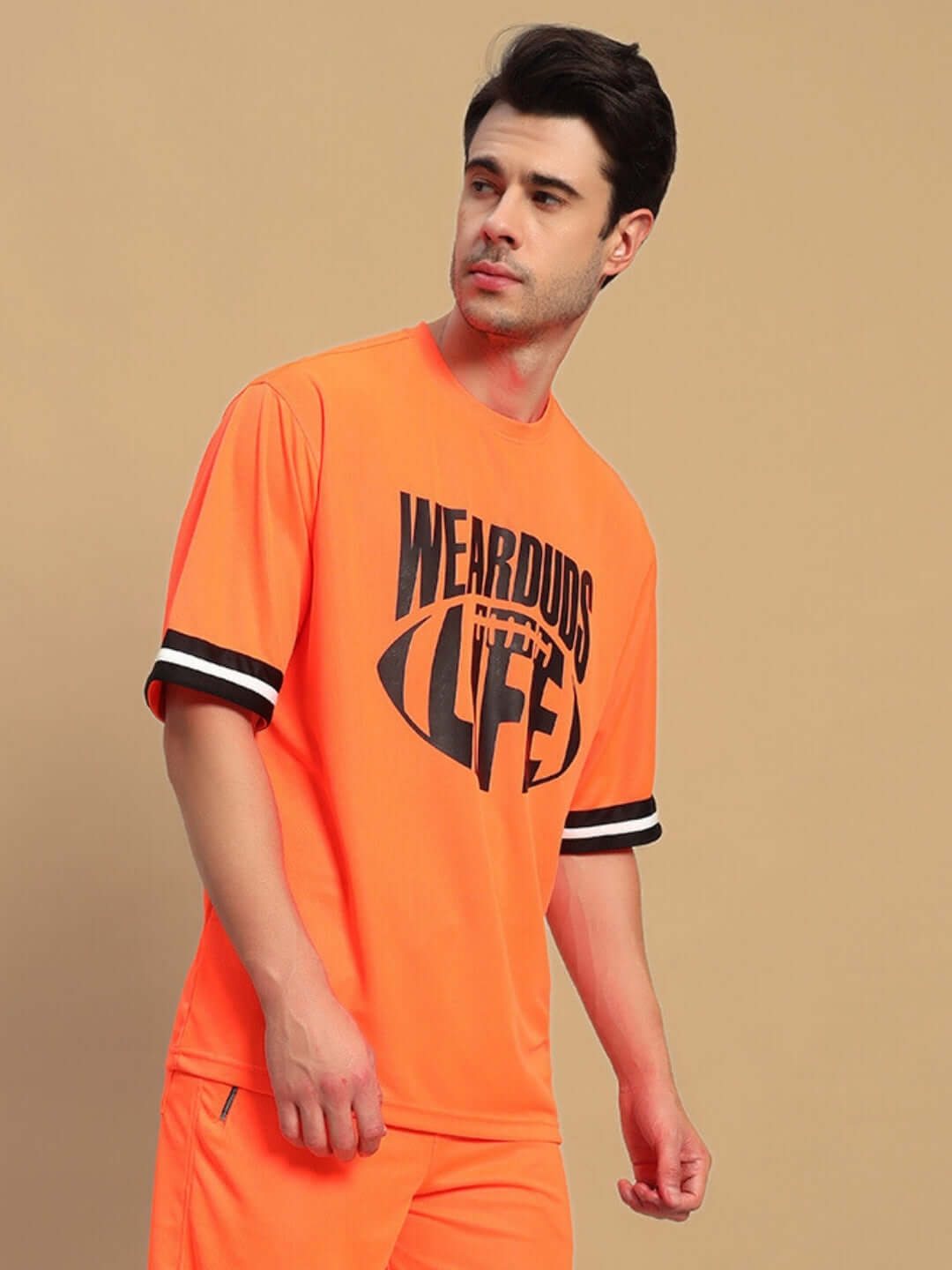 Man wearing orange oversized t-shirt with 'WEAR DUDS LIFE' print, featuring striped sleeves, custom fit option available for prepaid orders.