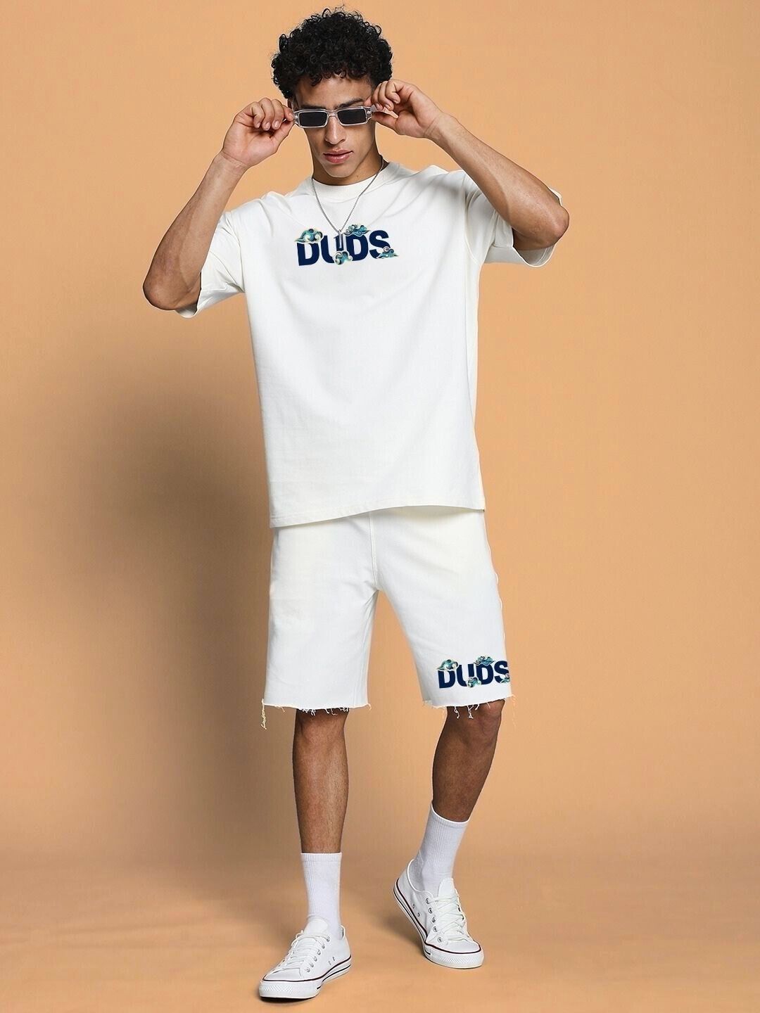 Model wearing CLOUD PRINTED RELAXED FIT SHORTS OFF WHITE, paired with matching off-white shirt and sunglasses, showcasing casual style.