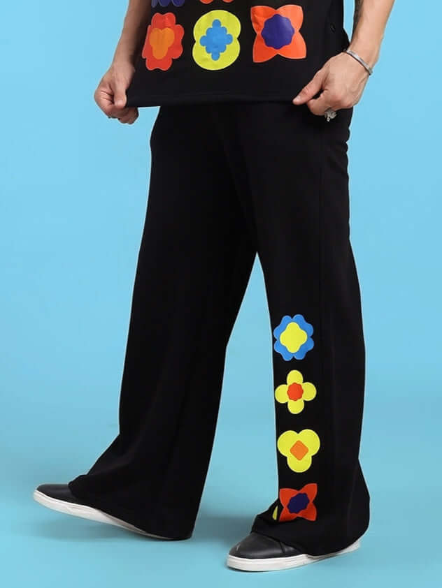 Black pants with colorful flower patterns worn by a person on a blue background.