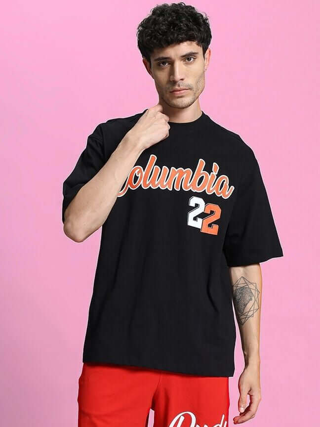 Model wearing Columbia 22 Print Over-Sized T-Shirt Black with bold graphic design on pink background.