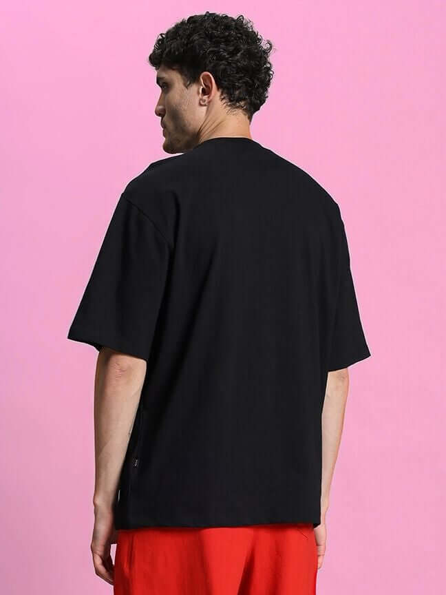 Back view of a person wearing a Columbia 22 Print Over-Sized T-Shirt Black against a pink background.
