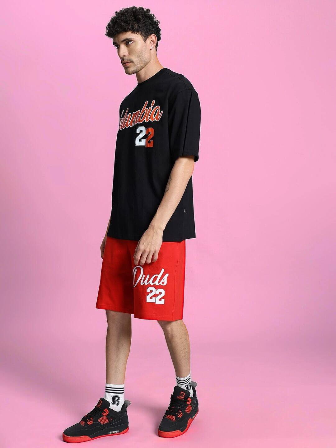 Model wearing COLUMBIA 22 PRINT SUMMER CO-ORD SET BLACK RED with oversized t-shirt and shorts against pink background.